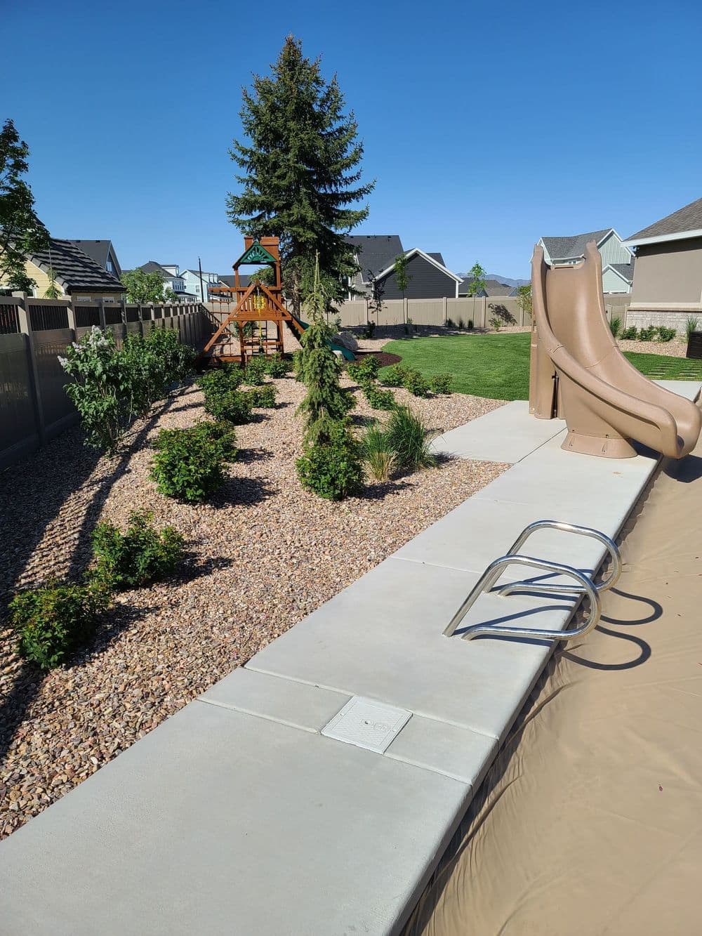 Backyard playground featuring a slide, climbing structure, and landscaped garden area.