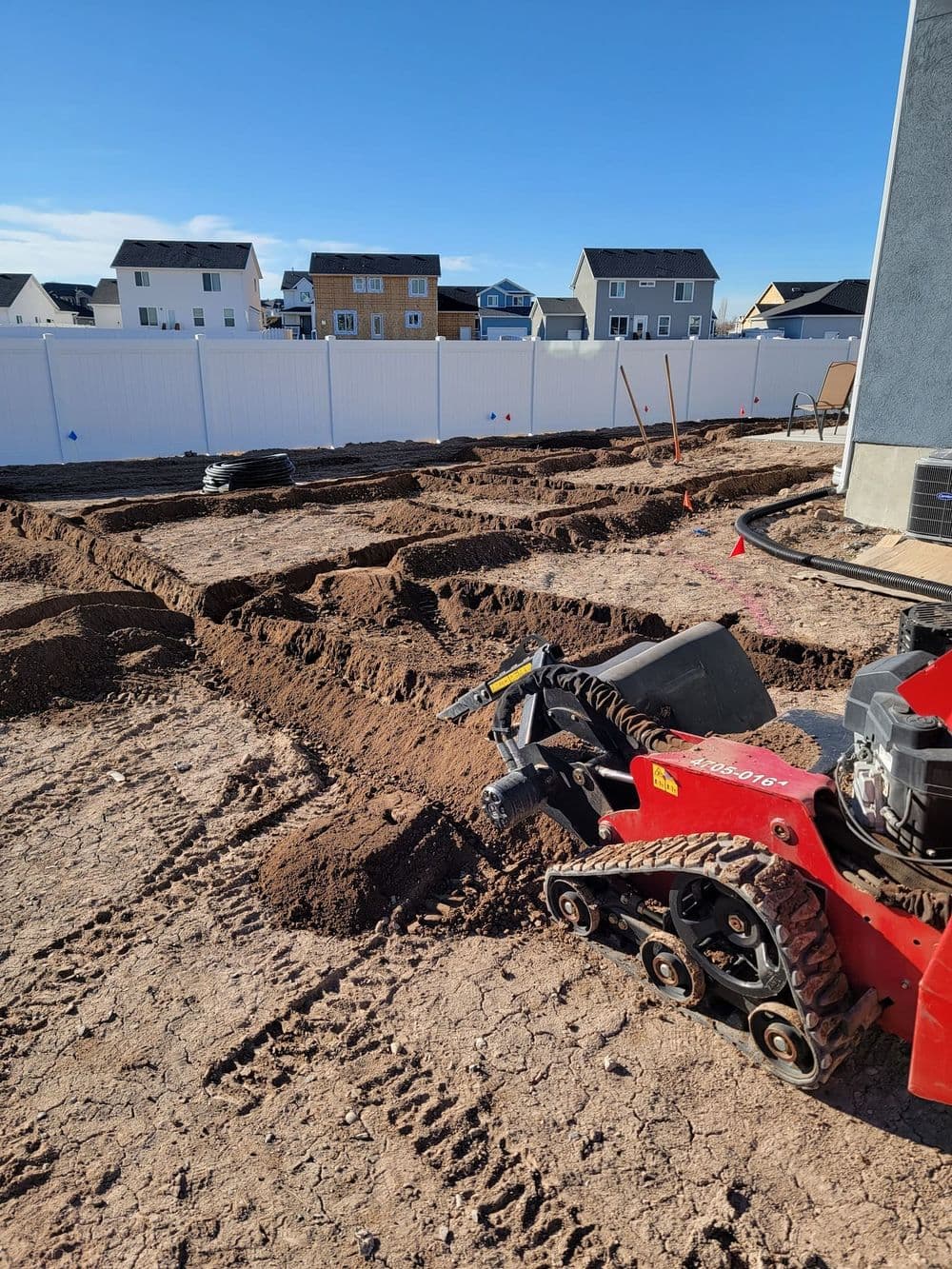 Construction site with soil prepared for landscaping, featuring a red tiller in the foreground.