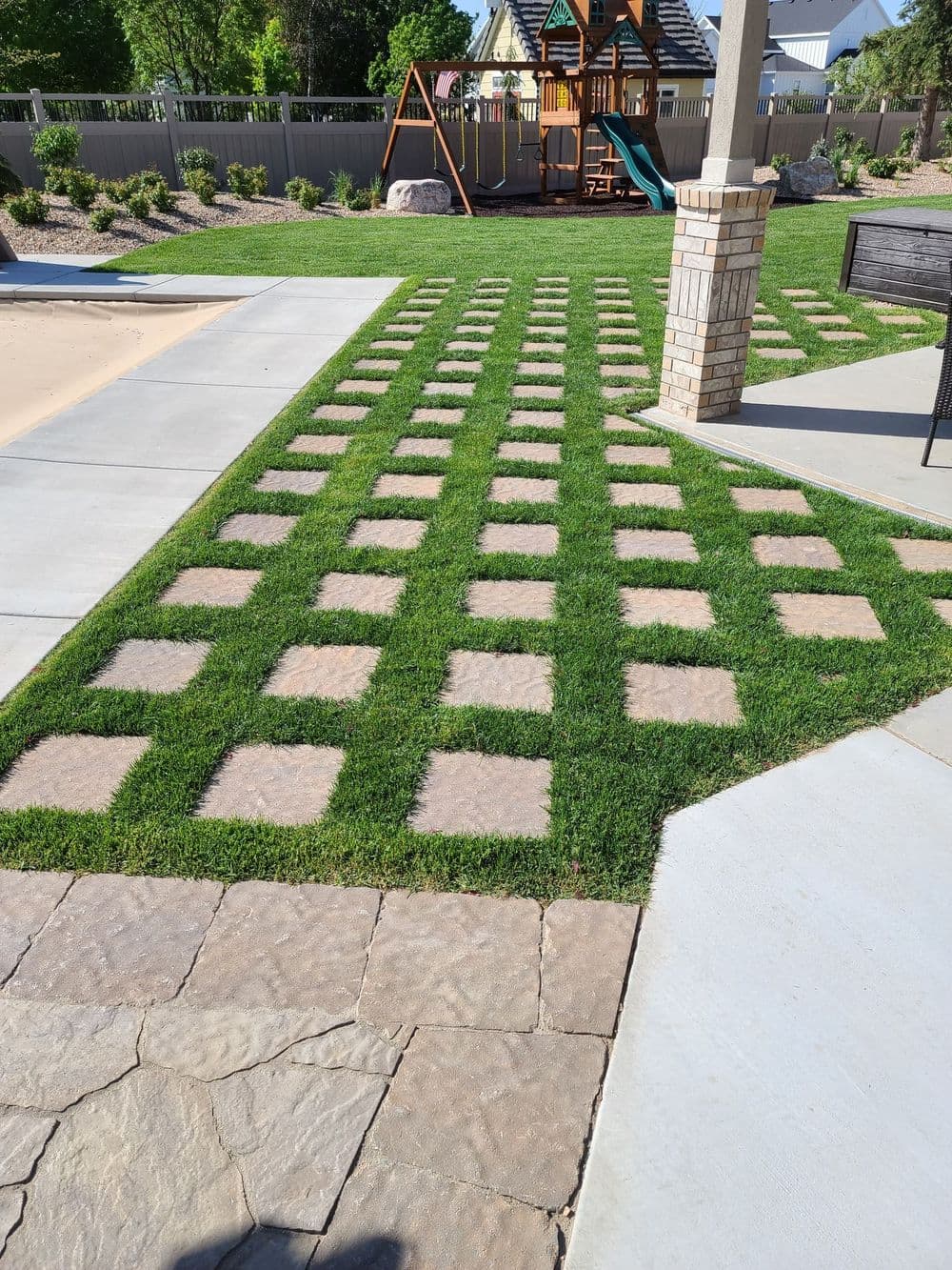 Lawn with grass and stone pavers arranged in a grid pattern, playground in background.