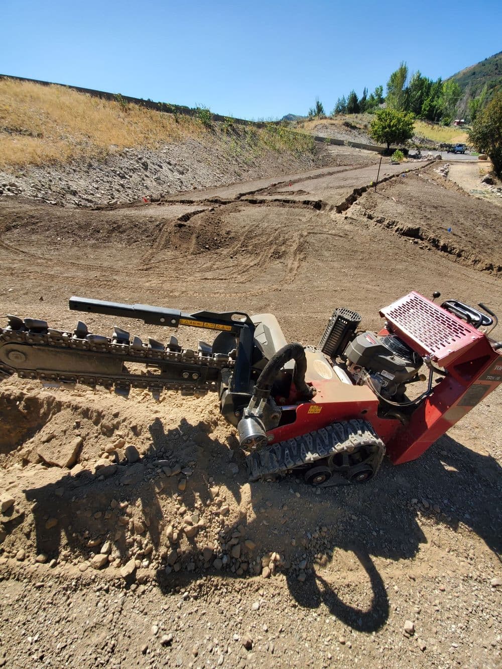 Mini excavator digging a trench on a construction site with clear blue sky in background.