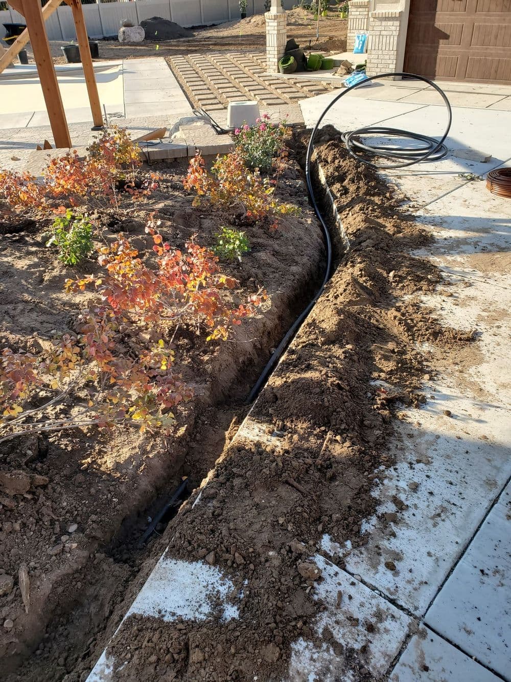 Trenched garden area with irrigation line and colorful shrubs in a landscape setting.
